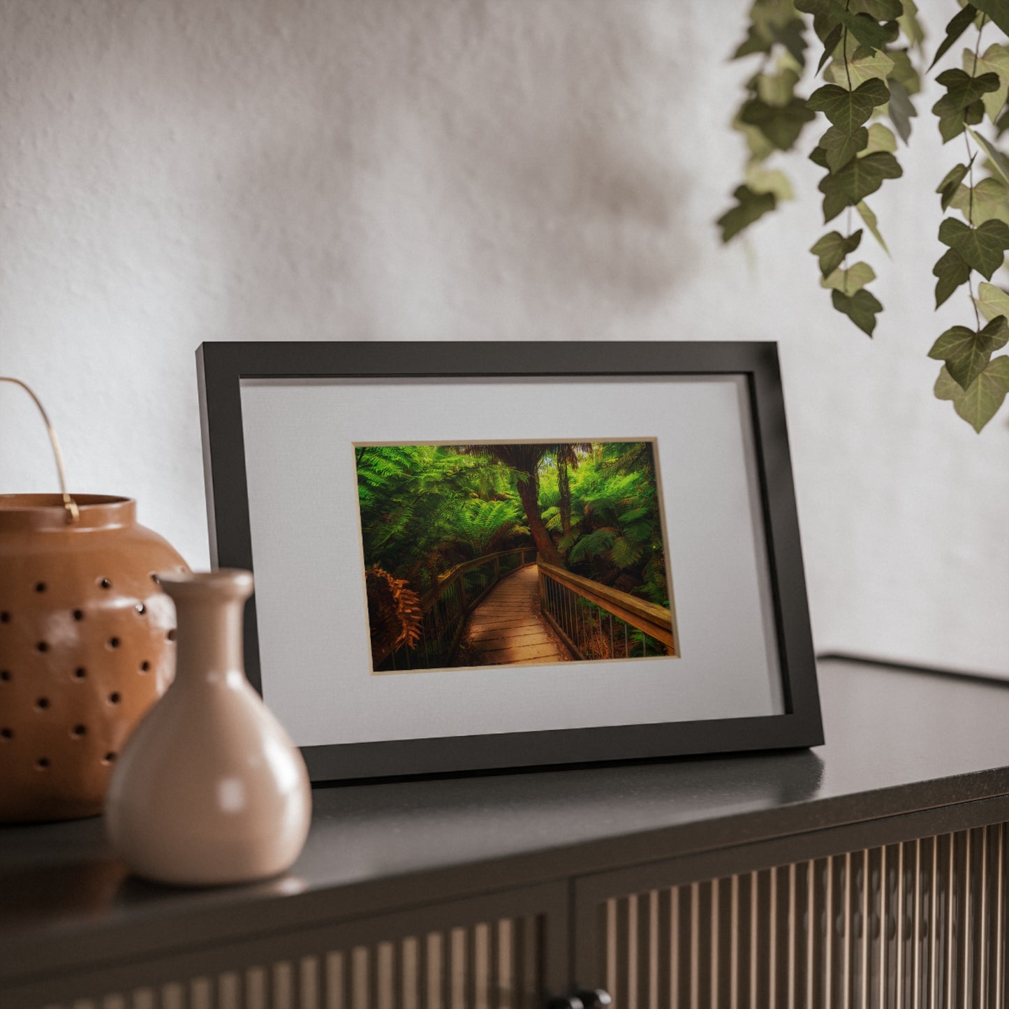 Wooden bridge winding through a lush forest of tall ferns printed black framed poster