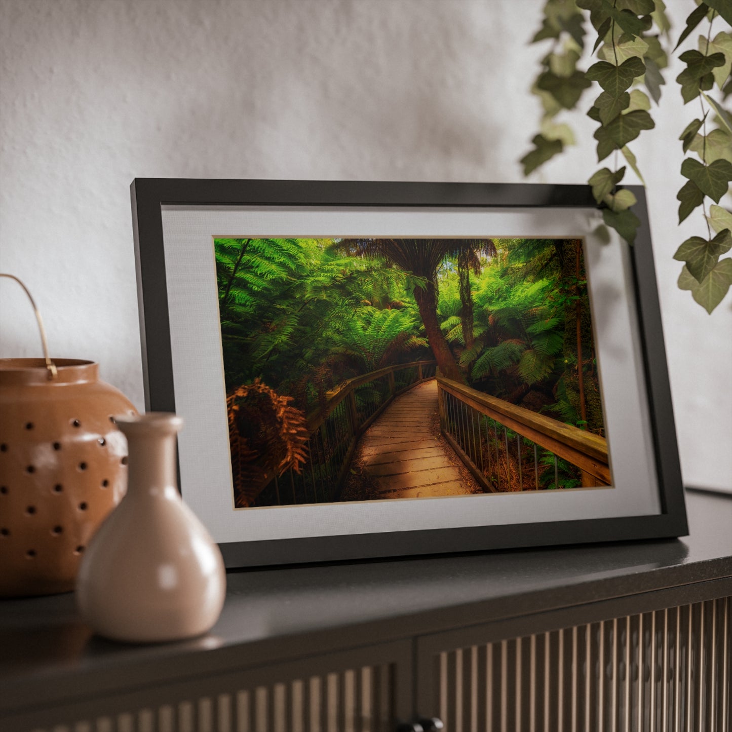 Wooden bridge winding through a lush forest of tall ferns printed black framed poster