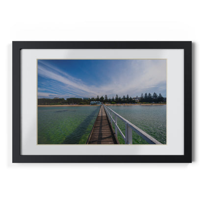 A beautiful jetty leading towards the shore over turquoise waters printed on a black framed poster