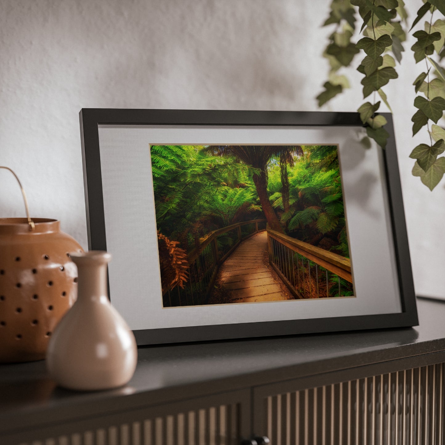 Wooden bridge winding through a lush forest of tall ferns printed black framed poster